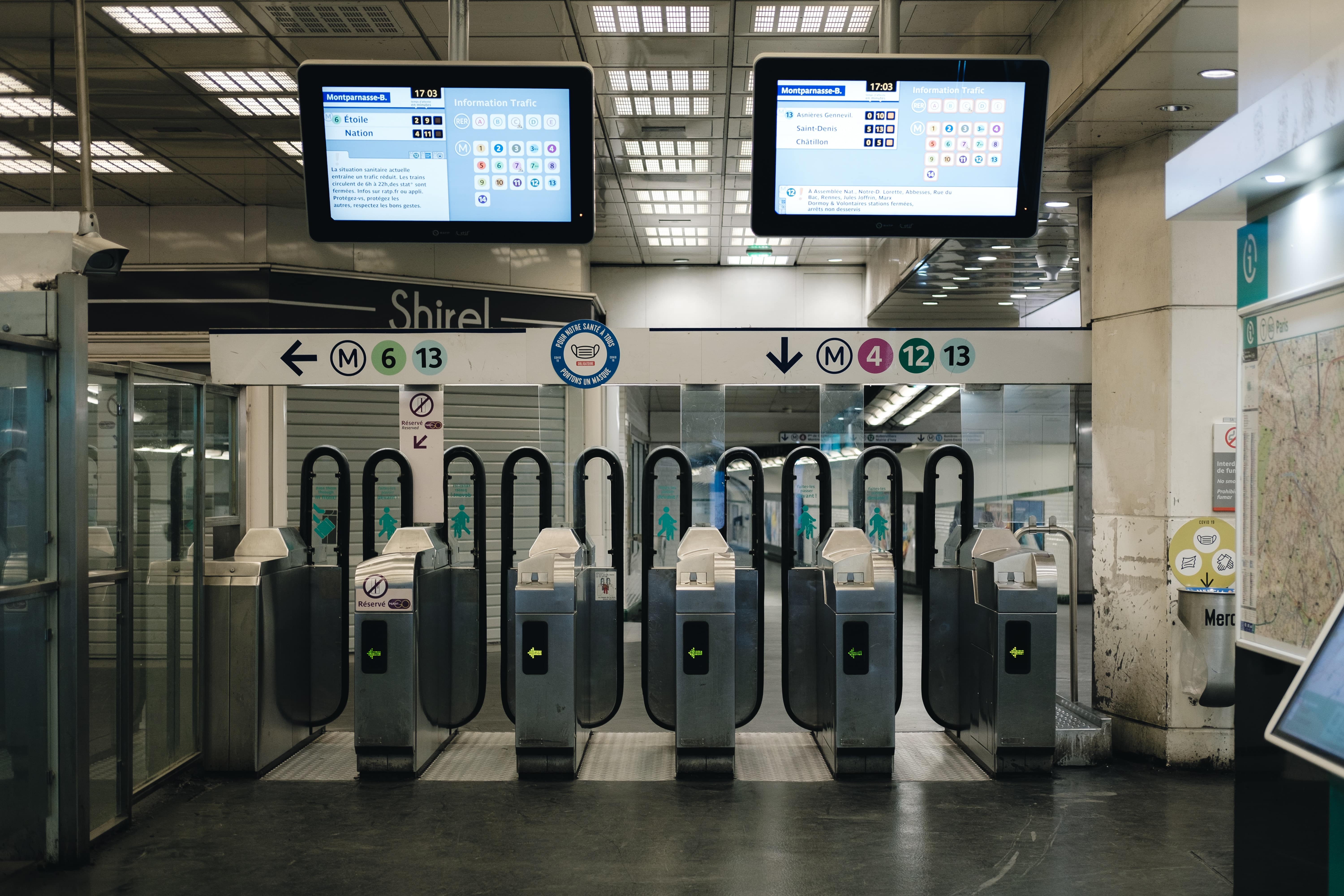 Station de métro avec des tourniquets et des panneaux d'information électroniques affichant les horaires et les lignes.