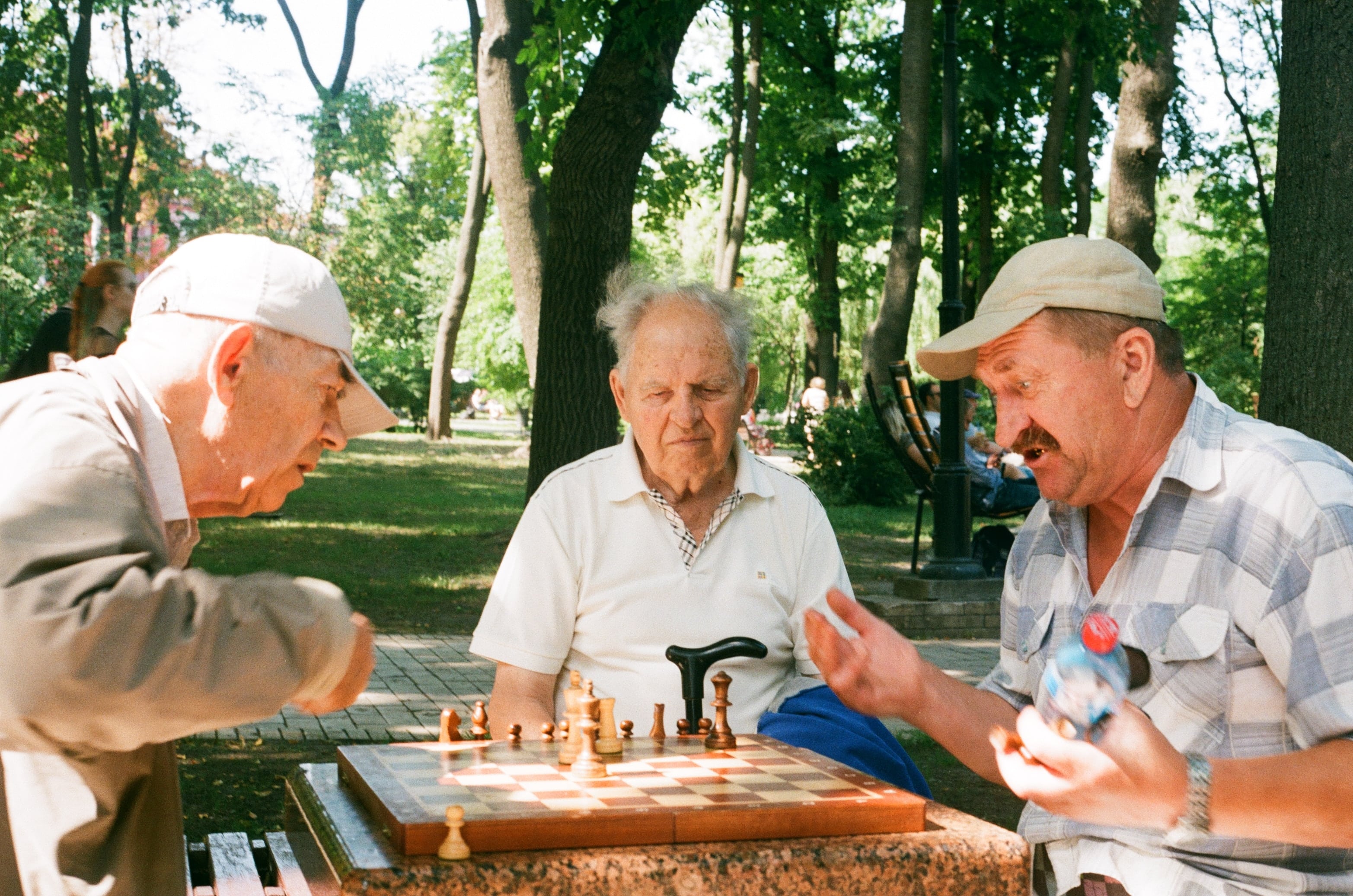 Trois hommes âgés jouant aux échecs dans un parc, illustrant le vieillissement de la population.